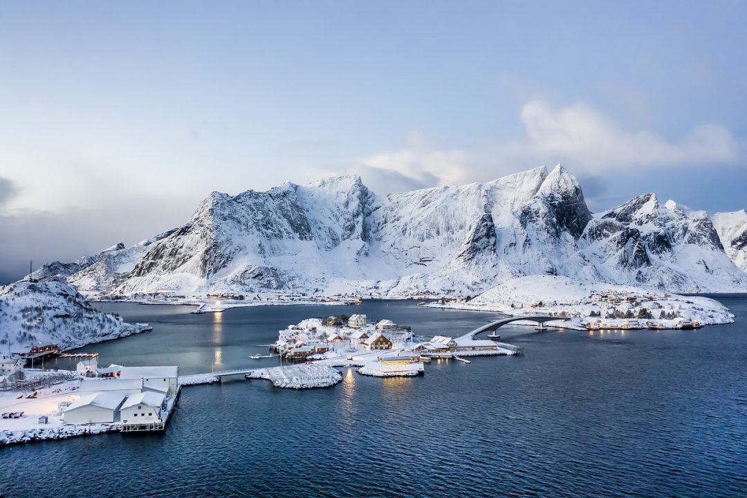 Snow-covered mountain range overlooking icy sea.
