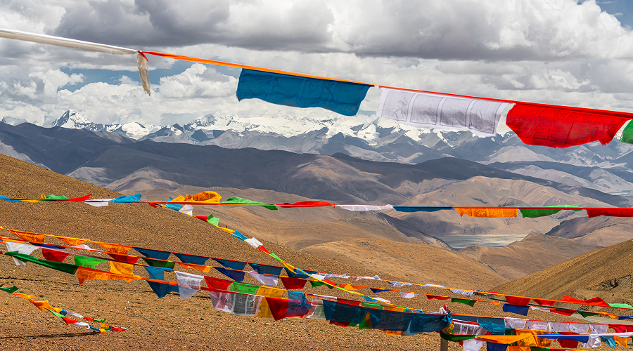 Tibetan prayer flags waving before distant snow-capped mountains.