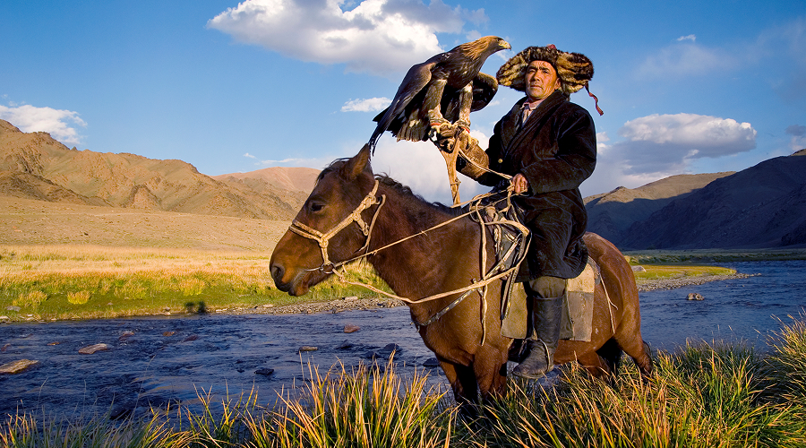 Kazakh eagle hunter on horseback near Altai mountain river.