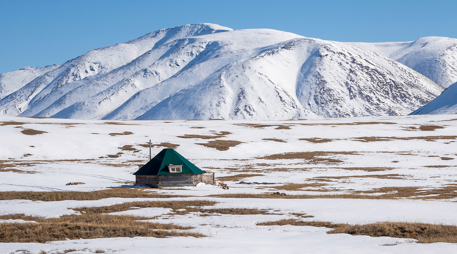 Wooden cabin sitting in snow beneath majestic winter mountains.