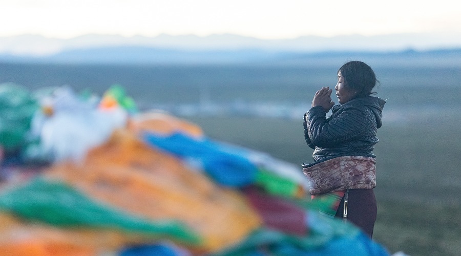 Devotee praying near colorful flags at Mount Kailash sacred peak.