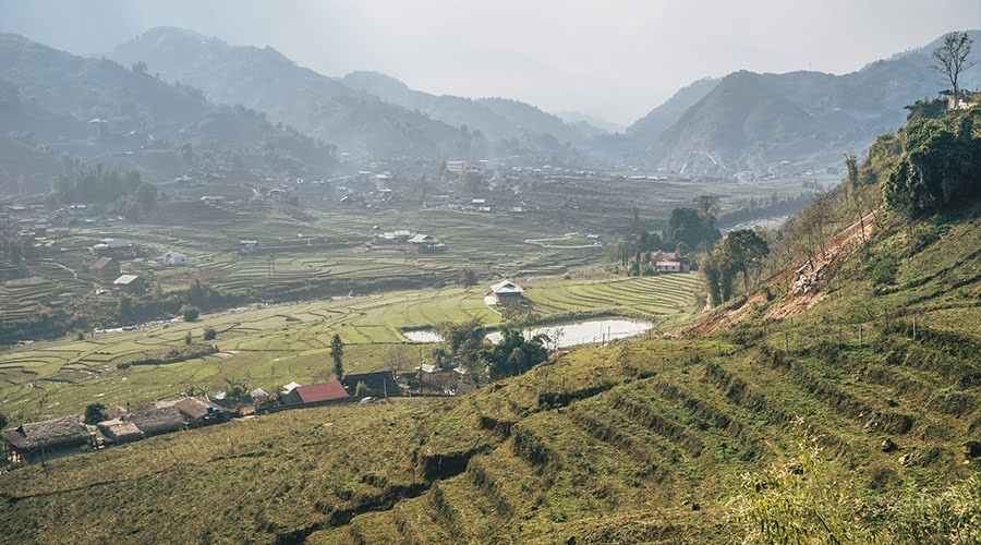 Mist-shrouded green valley with terraced agricultural fields.