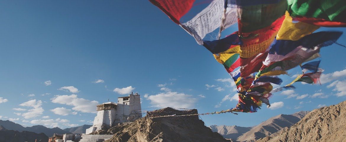 Tibetan prayer flags flying near a historic hillside monastery.