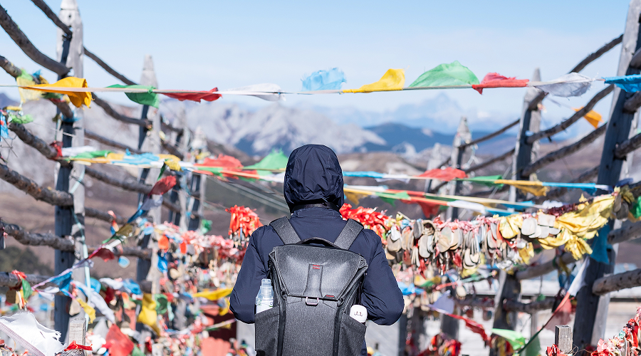 Traveller walking through colourful prayer flags on a mountain pass.