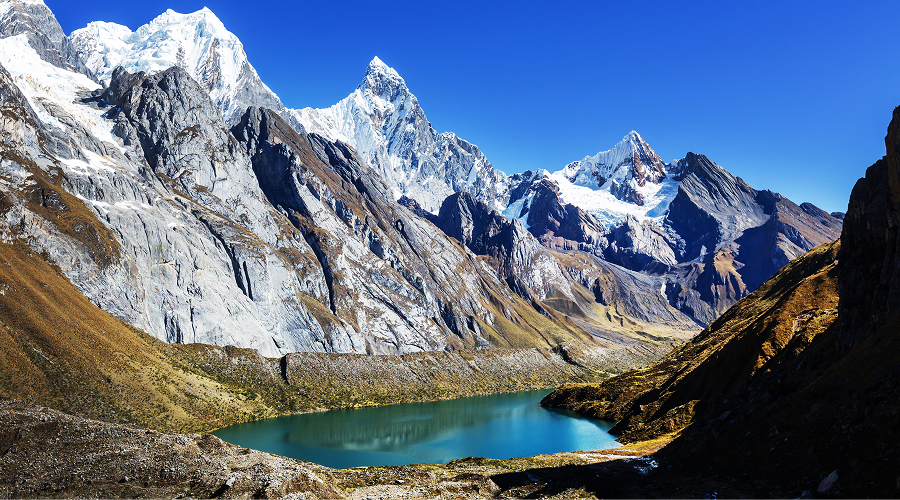 Turquoise alpine lake beneath snow-capped Himalayan mountain peaks.