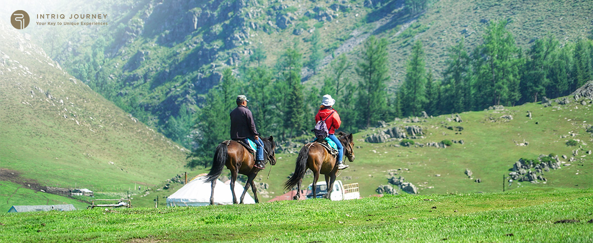 Two travelers riding horses through green mountain valley.